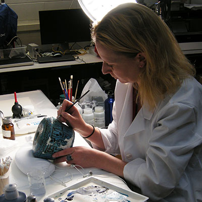 Christie Pohl working on a vase with a brush