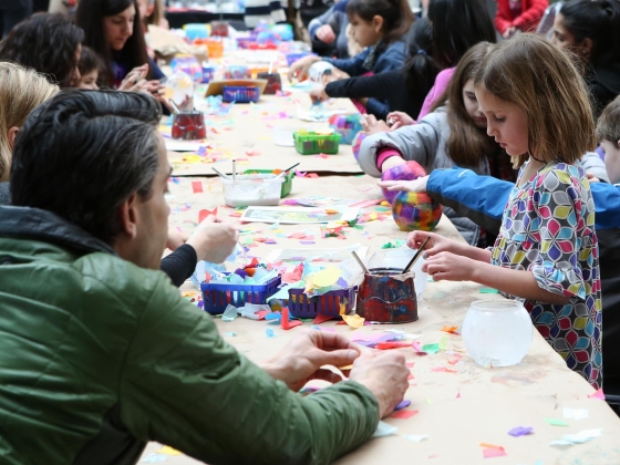 Young visitor decorating plastic bowl at long row of table surrounded by families Young visitor decorating plastic bowl at long row of table surrounded by families