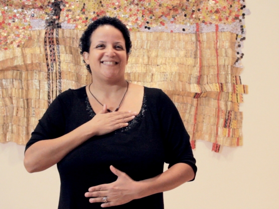 Woman signing American Sign Language in front of artwork on wall Woman signing American Sign Language in front of artwork on wall