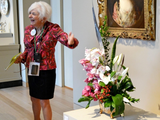 Art in Bloom Tours Guide discussing floral arrangement set in front of painting