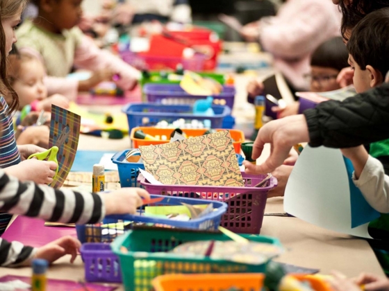 Hands reaching into plastic baskets of patterned paper, spread down center of long table