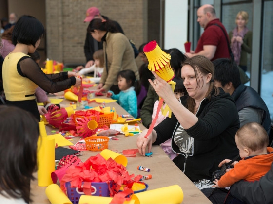 Visitor sitting next to baby holding yellow lantern made of construction paper Visitor sitting next to baby holding yellow lantern made of construction paper