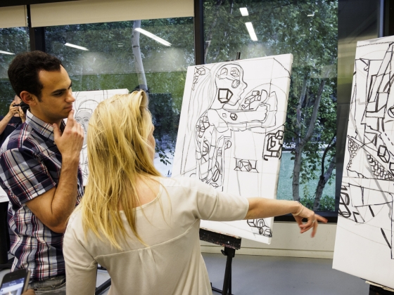 Woman pointing at drawing on easel with man looking onwards Woman pointing at drawing on easel with man looking onwards