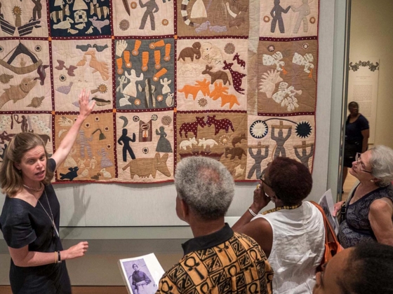 Guide discussing Harriet Powers' Pictorial Quilt in front of tour group