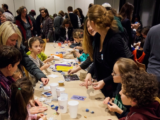 Youths and adults standing at long table making dreidels Youths and adults standing at long table making dreidels