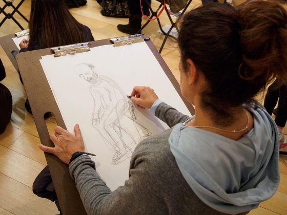 Woman sketching a bearded man sitting on large drawing pad Woman sketching a bearded man sitting on large drawing pad