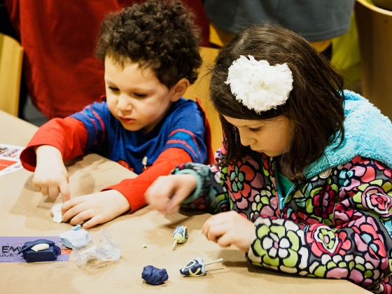 Children standing at table making dreidels out of clay Children standing at table making dreidels out of clay