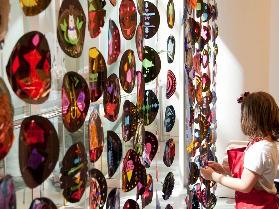 Girl adjusting to circle of colored stained glass cellophane hanging in front of window Girl adjusting to circle of colored stained glass cellophane hanging in front of window