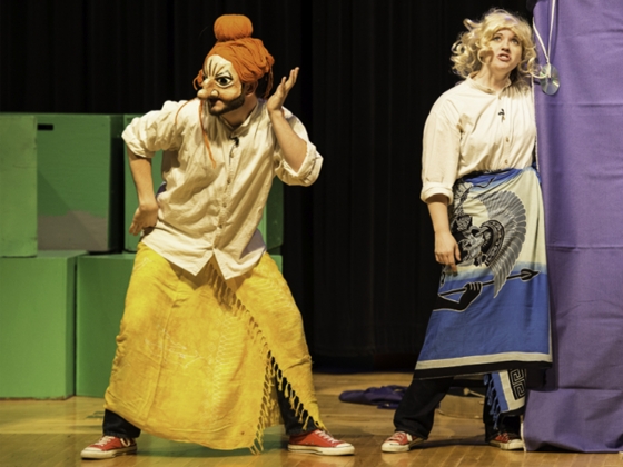 MythMasters - Masked actor performs on stage in front of actor in wig MythMasters - Masked actor performs on stage in front of actor in wig