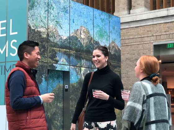 Three visitors holding cups standing in front of elevators in Shapiro Family Courtyard