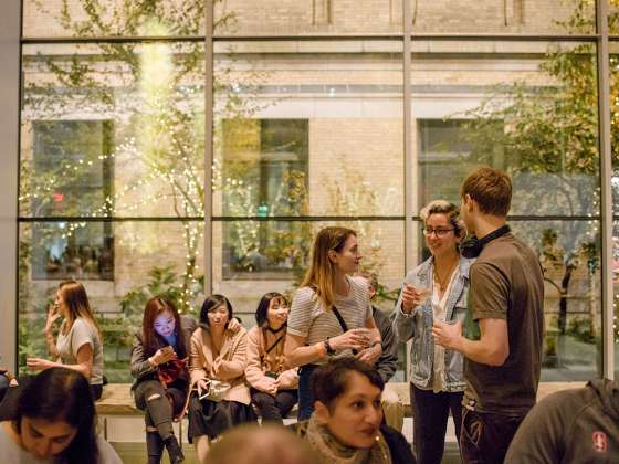 Three visitors with drinks in hand standing in Shapiro Family Courtyard during First Friday event with other attendees seated nearby