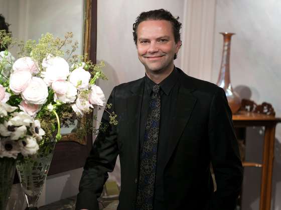 Remco van Vliet in dark suit standing by floral arrangement in glass vase